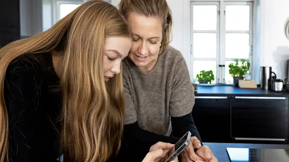 En voksen og et barn kigger på en mobiltelefon.